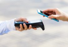 Płatność zbliżeniowa telefonem: kobieta przykłada smartfon do terminala płatniczego.